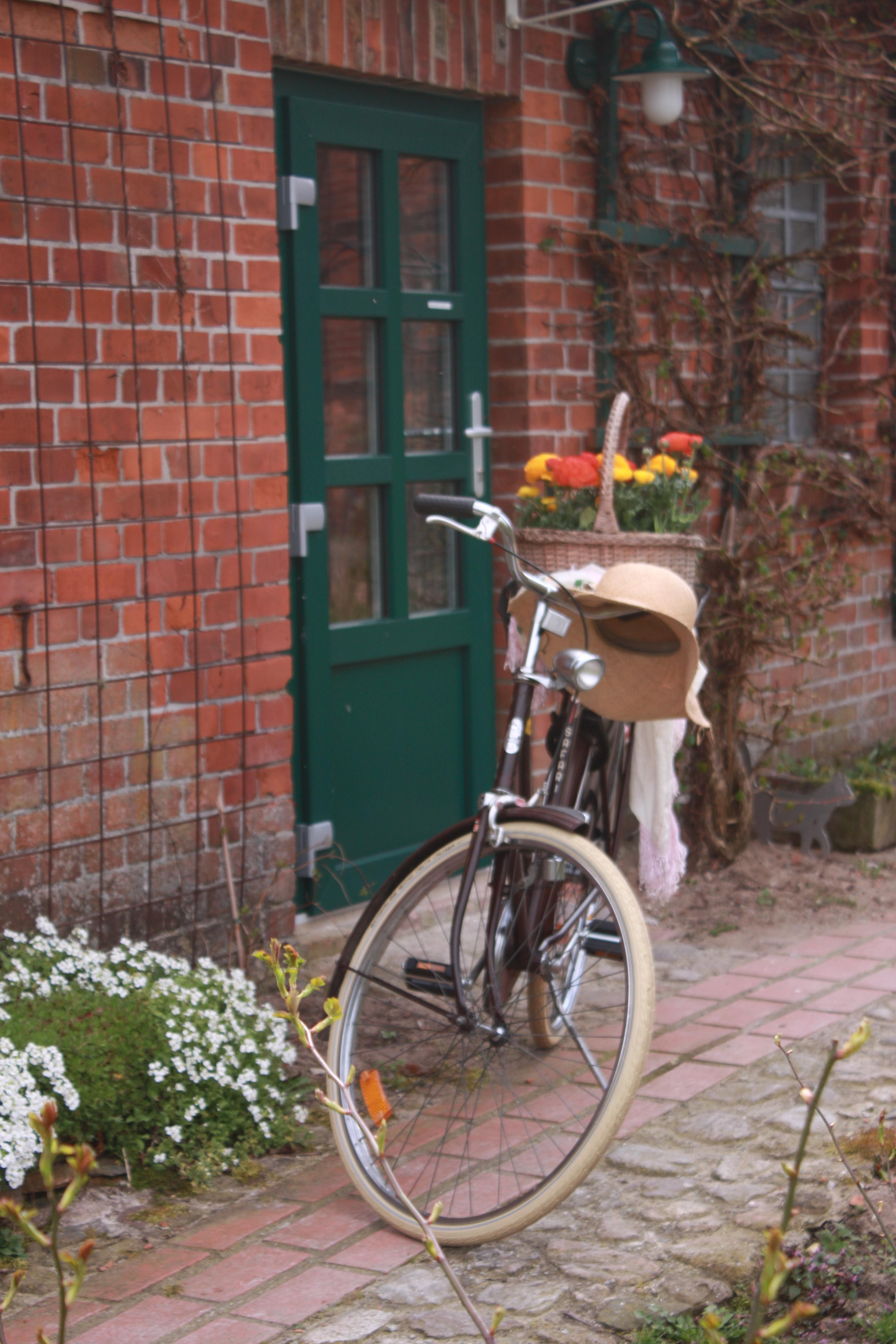 das Bild zeigt ein Fahrrad vor dem Eingang der Pension im Privelacker Paradiesgarten. Auf dem Gepäckträger steht ein Korb mit bunten Blumen, am Lenker hängt ein sommerlicher Strohhut.